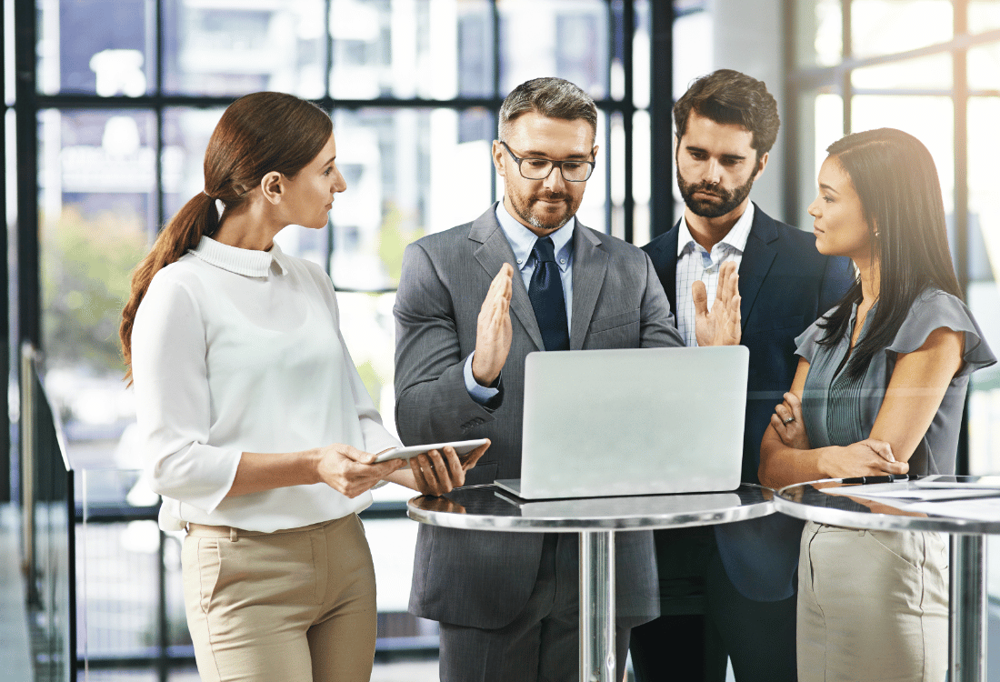 Four professionals in a modern office with a laptop, with the central man explaining how to fuel growth with an SME working capital loan.